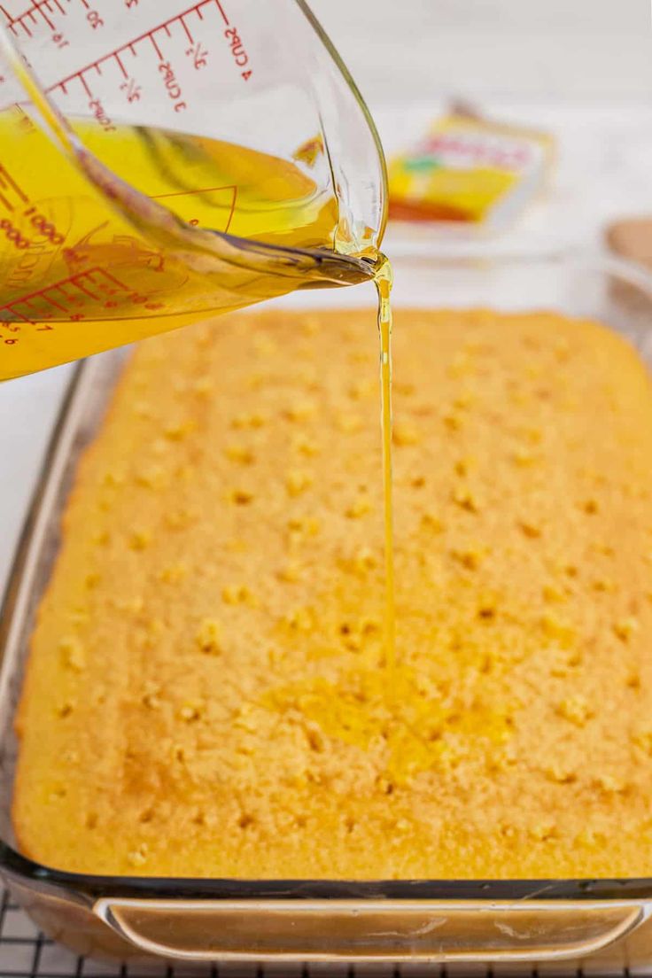 someone pouring oil on top of a cake in a glass pan with a measuring cup