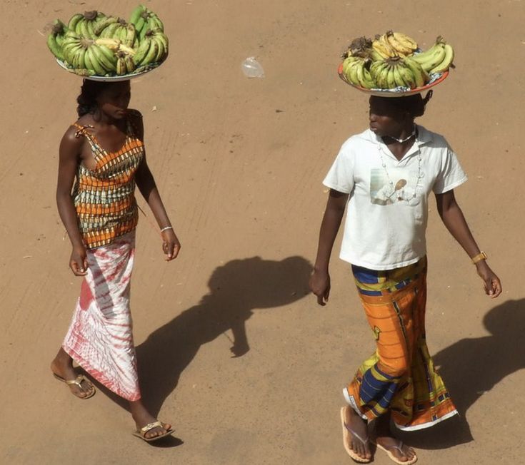 two women walking down the street carrying bananas on their heads