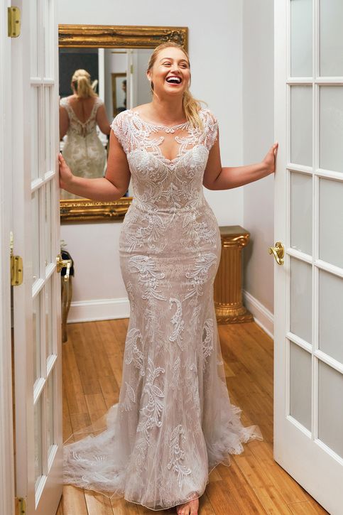 a woman standing in front of a mirror wearing a wedding dress and smiling at the camera