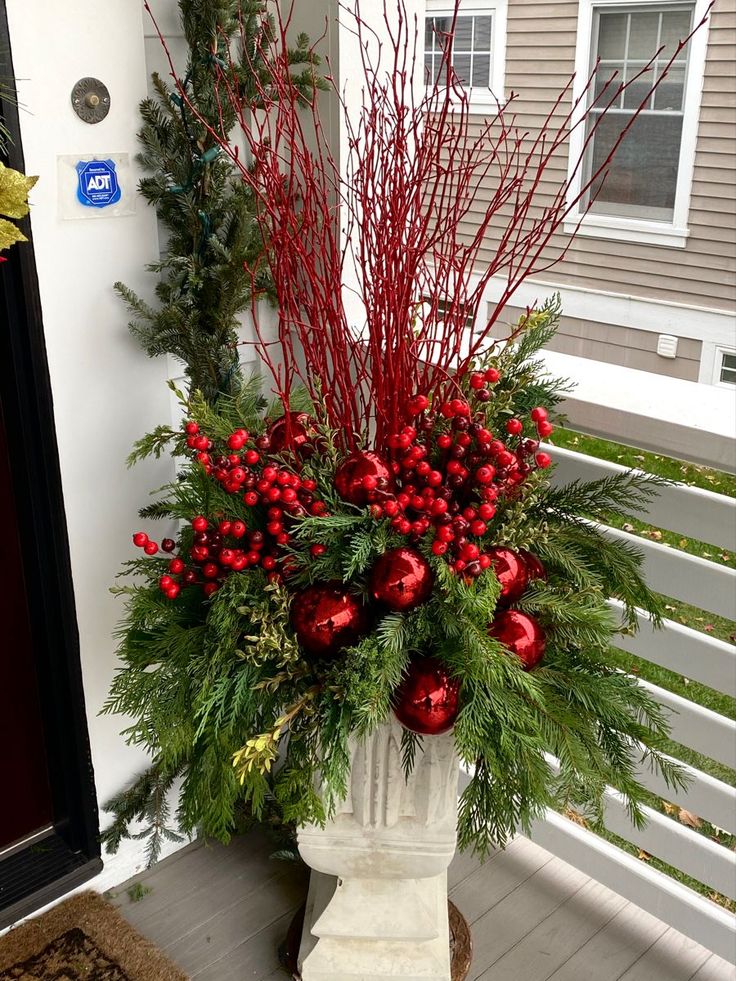 a planter filled with red berries and greenery on the front porch for christmas