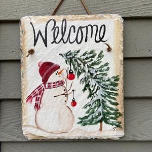 a welcome sign with a snowman and pine tree on the side of a house