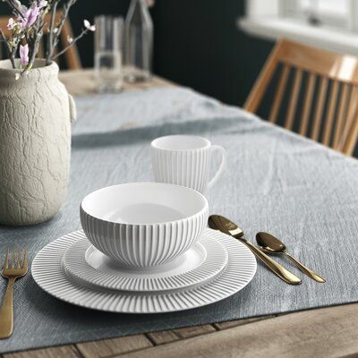 the table is set with white dishes and gold utensils