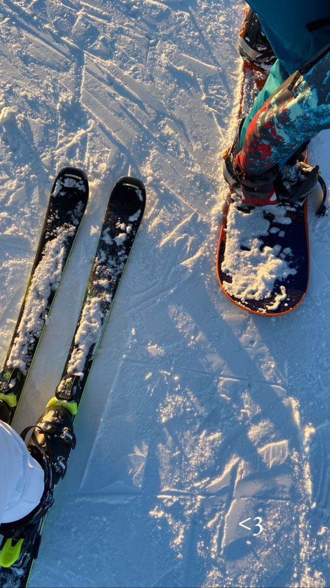 two pairs of skis sitting on the snow next to each other in front of a person's feet