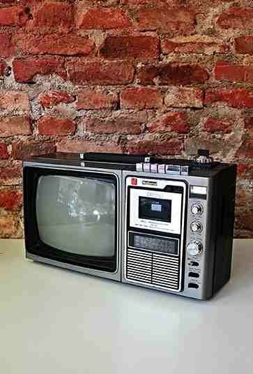 an old fashioned television sitting on top of a table next to a brick wall and vase