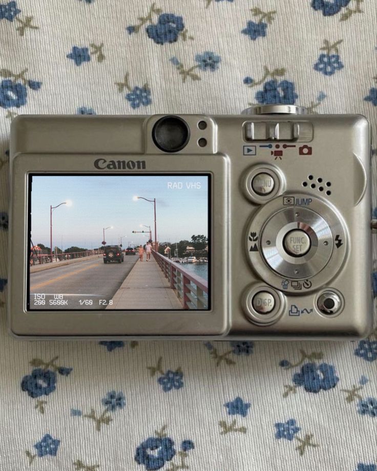 a digital camera sitting on top of a flowered cloth covered tablecloth next to a window