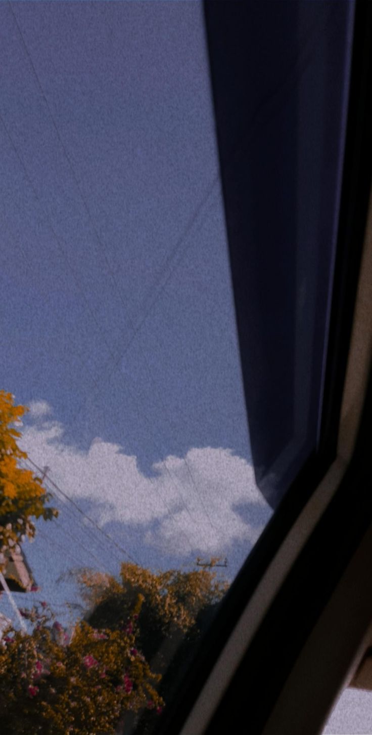 a clock tower seen through the window of a vehicle's side view mirror, with trees and clouds in the background