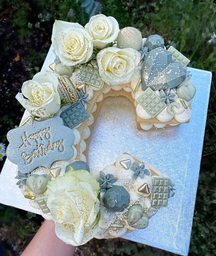 a hand holding a cake decorated with white roses and frosting on top of it