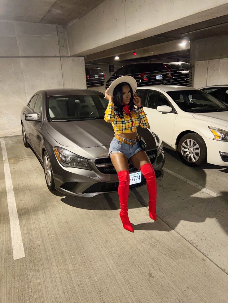 a woman in short shorts and red boots standing next to a car