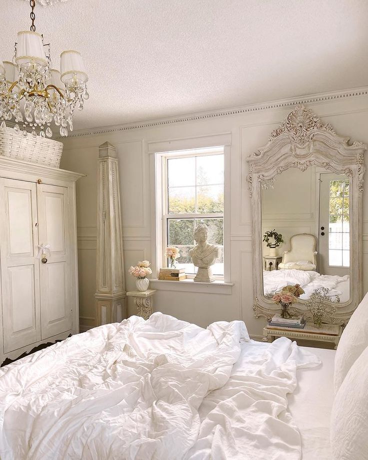 a white bed sitting in a bedroom next to a window with a chandelier