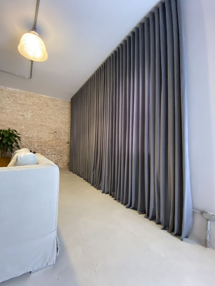 a living room filled with furniture next to a wall covered in grey curtained drapes