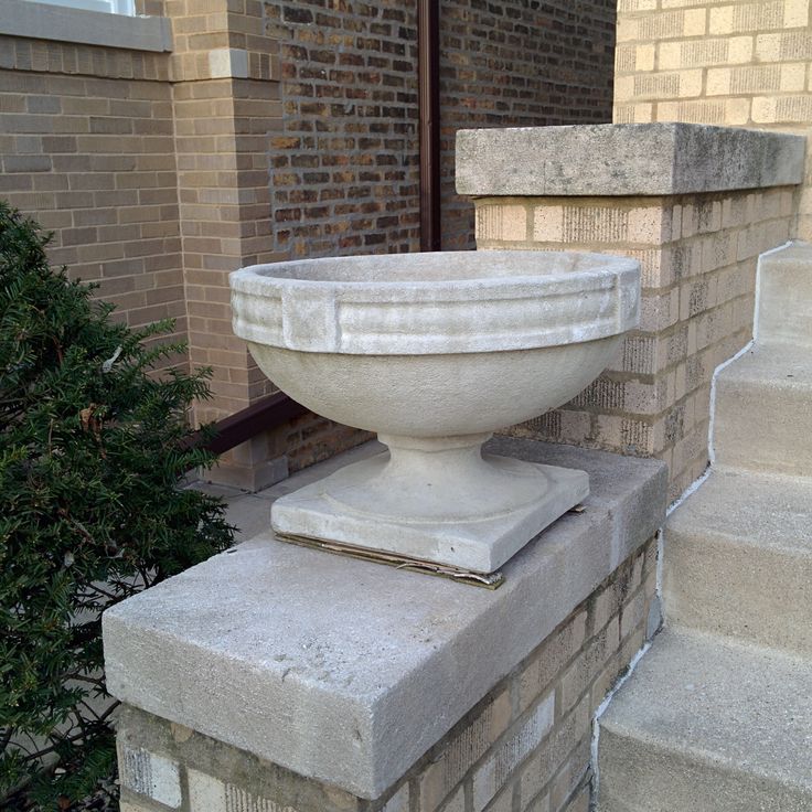 a large white bowl sitting on top of a cement pillar next to a tree in front of a brick building