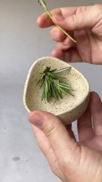 a person is holding a small bowl with some herbs in it and there are two hands