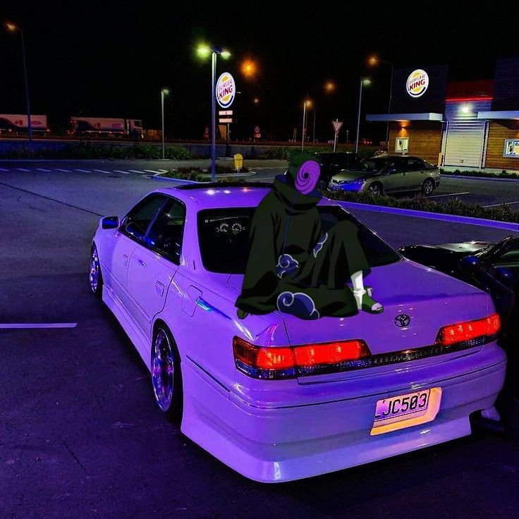 a person in a hoodie sitting on the back of a purple car at night