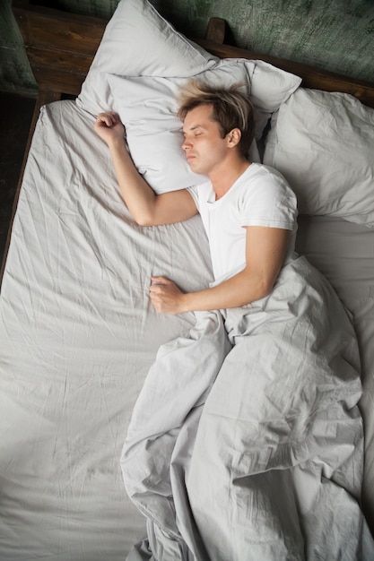 a man laying in bed with his eyes closed and arms tucked under the pillow as he sleeps