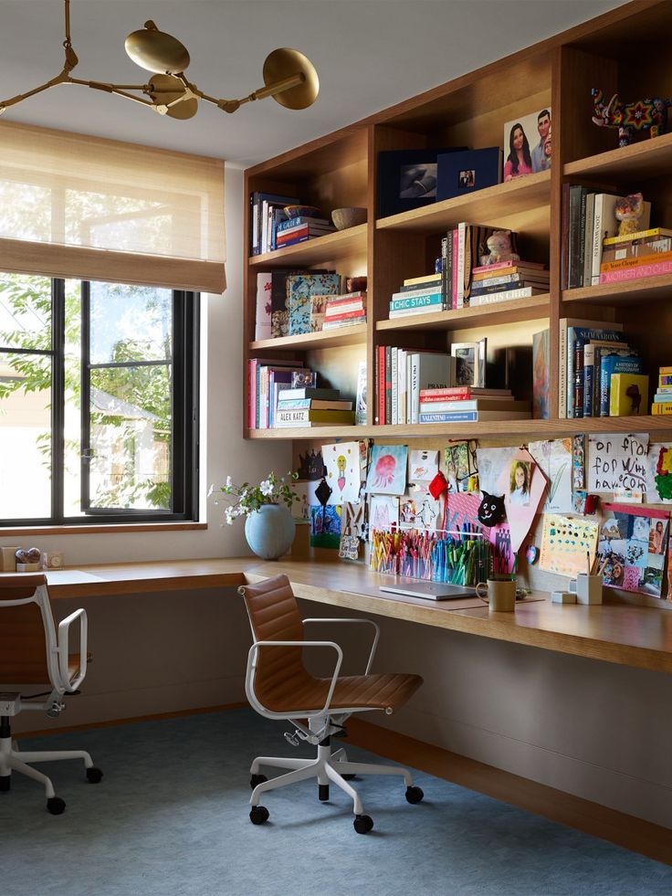 a desk with two chairs and bookshelves in front of a window