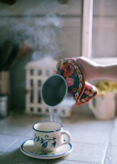 someone is pouring tea into a cup on the kitchen floor with their hand reaching for it