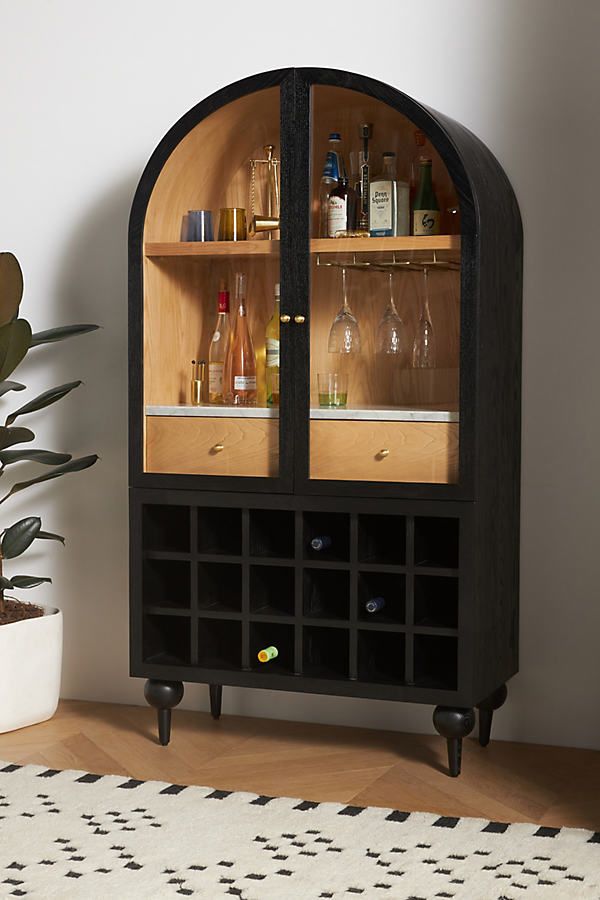 a black cabinet with wine glasses and liquor bottles on the top, in front of a potted plant