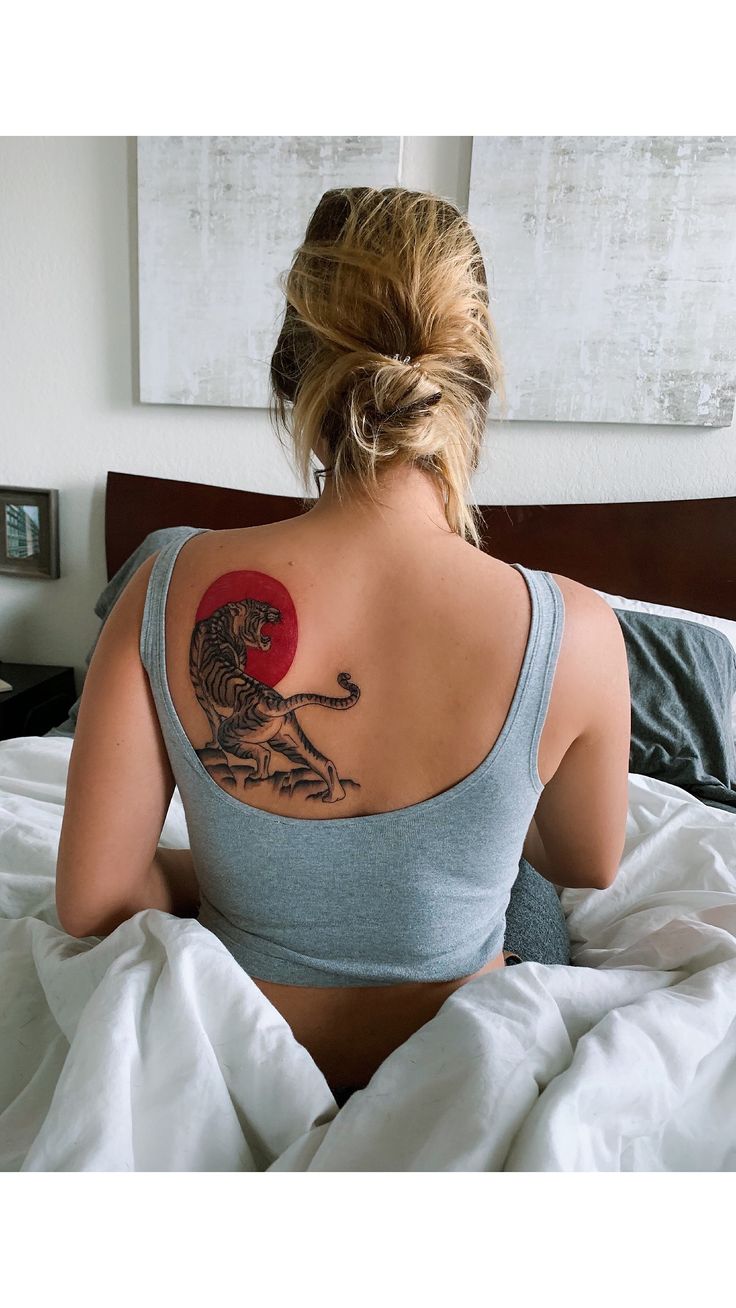 a woman with a tattoo on her back sitting in bed