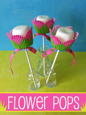 four pink and green flower pops in a clear glass vase on a yellow tablecloth