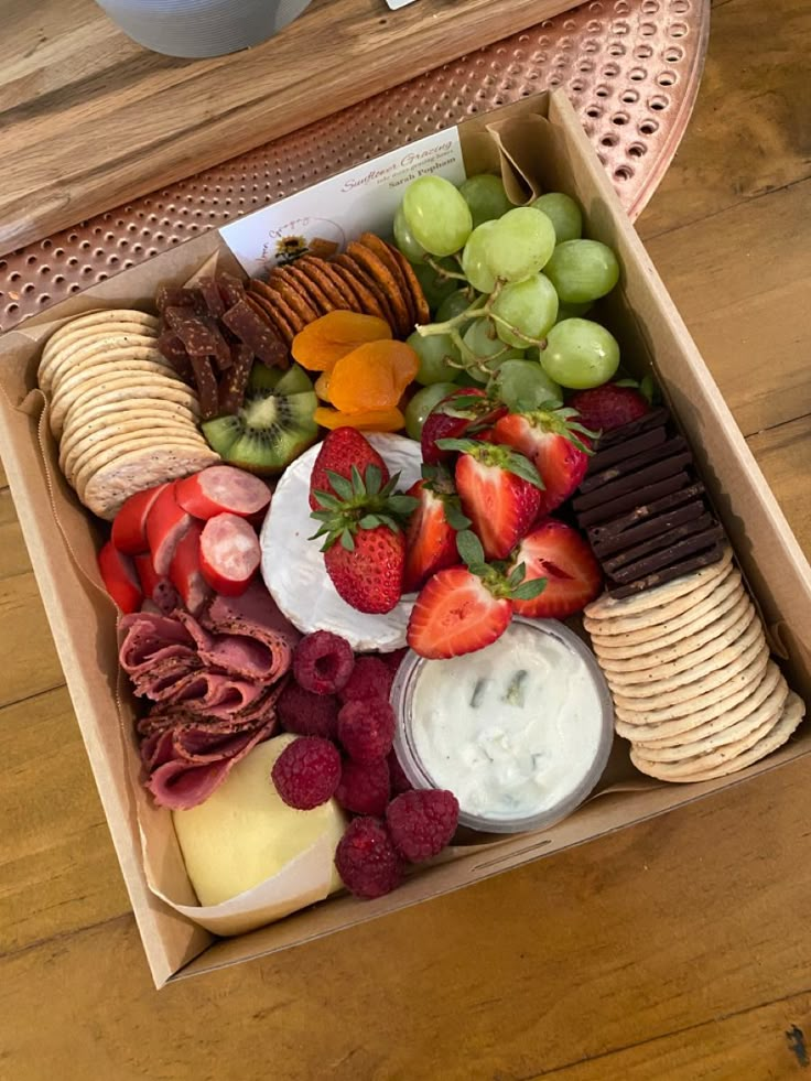 a box filled with assorted fruit and crackers on top of a wooden table