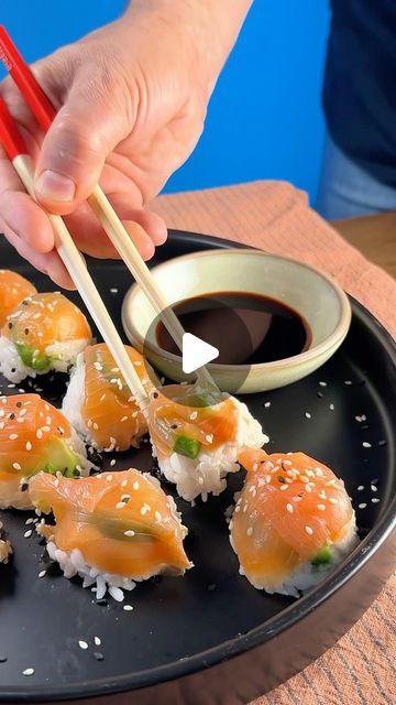 someone holding chopsticks over sushi on a black plate