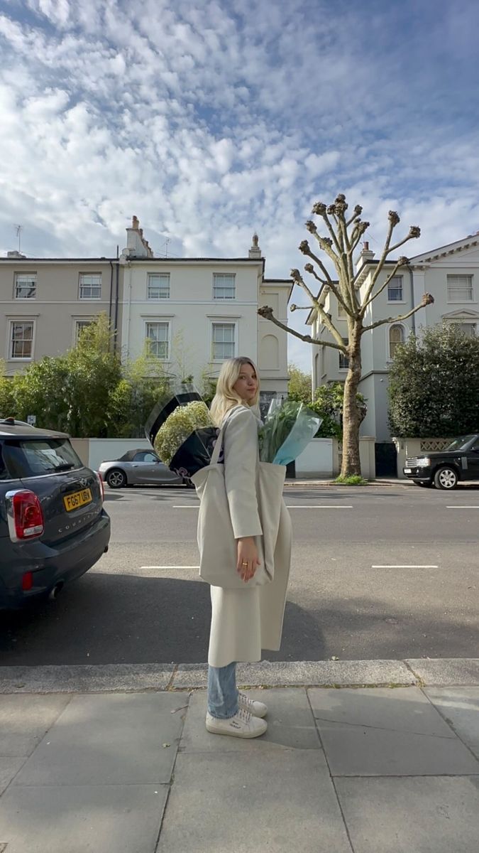 a woman is standing on the sidewalk with her umbrella open and looking up at something in the sky