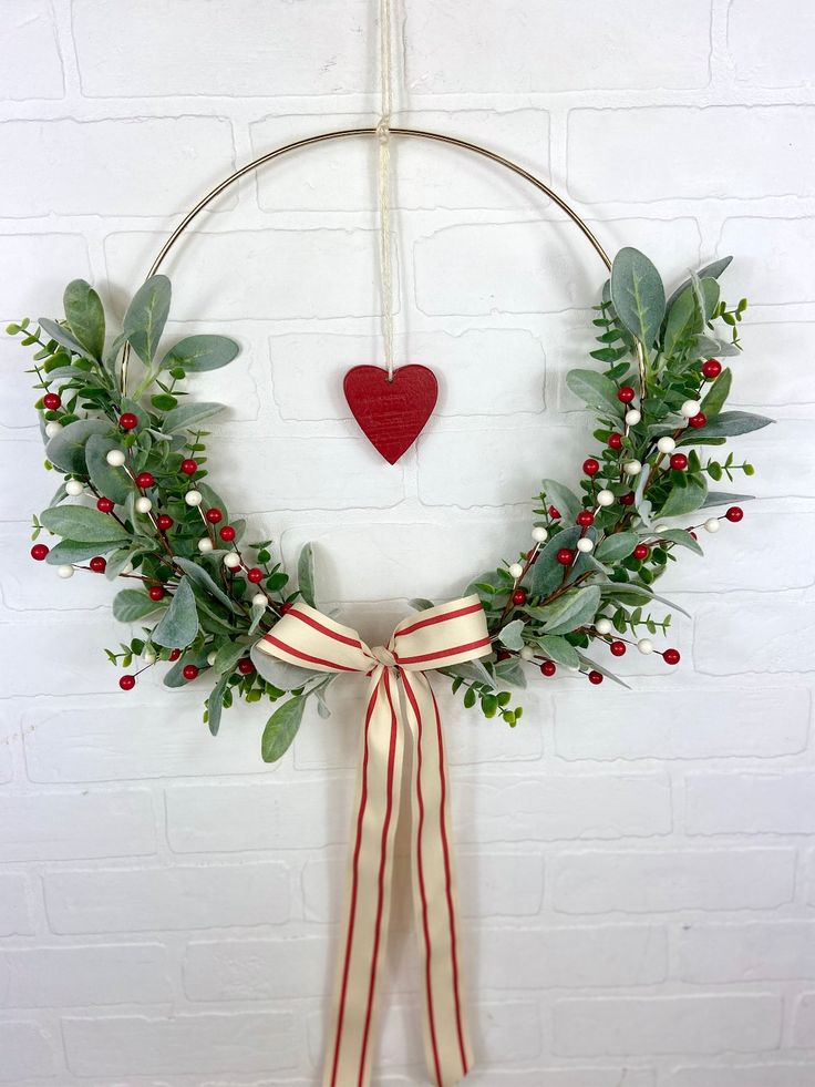 a wreath hanging on the wall with red berries and greenery around it, decorated with a heart