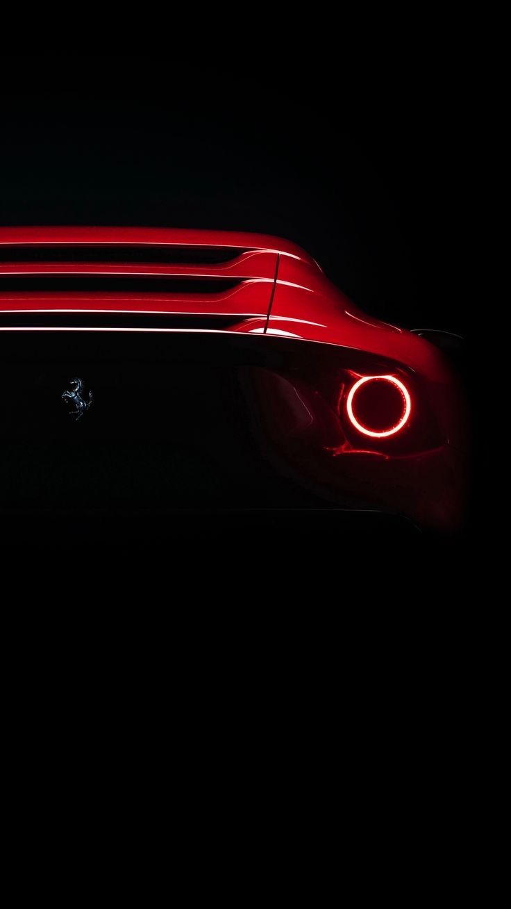 the rear end of a red sports car with its lights turned on in the dark