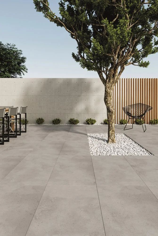 an empty patio with tables and chairs next to a tree in front of a wall