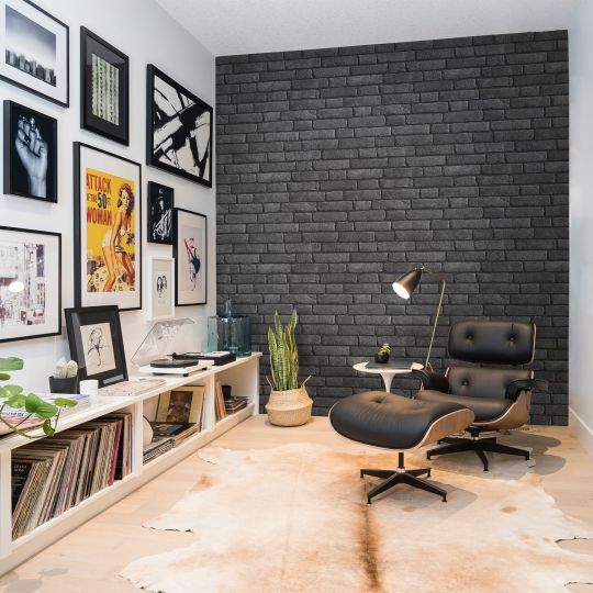 a living room with black brick wall and white carpeted flooring, an office chair in front of a bookcase filled with books