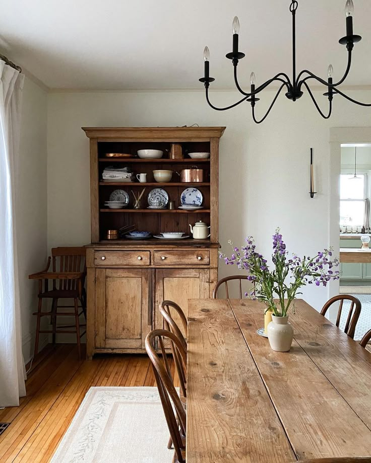 a dining room table and chairs in front of a wooden hutch with dishes on it