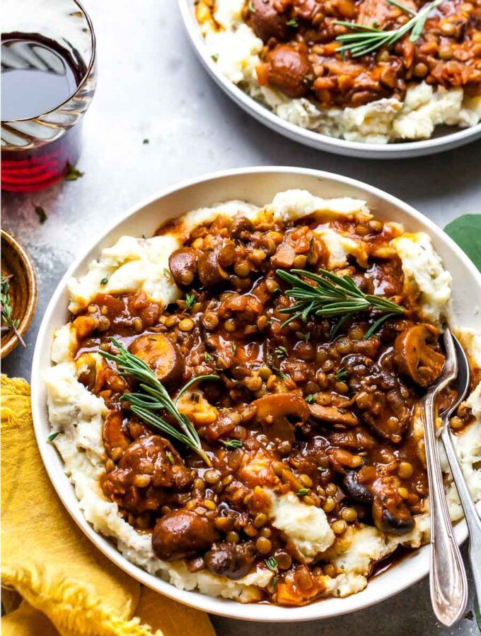 two bowls filled with mashed potatoes covered in meat and gravy next to a glass of water