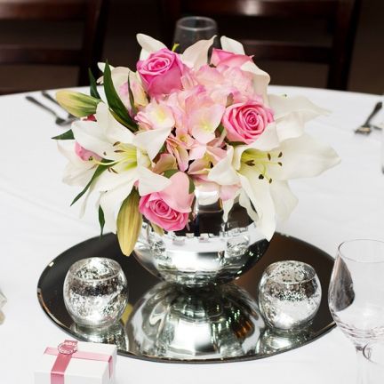 a vase with pink roses and white lilies on a silver platter at a table