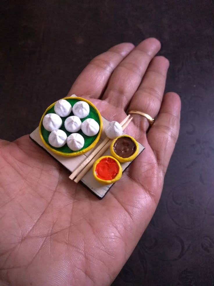 a person's hand holding a miniature food dish with chopsticks and marshmallows