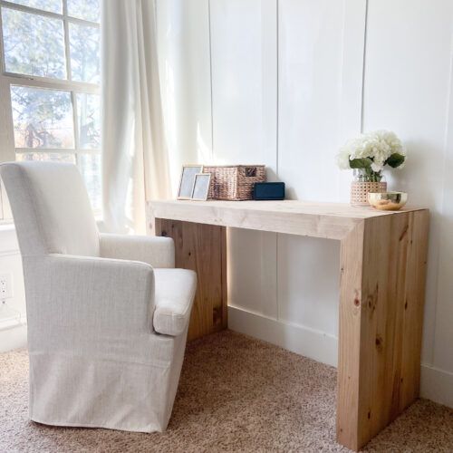 a white chair sitting next to a wooden desk in front of a window with curtains