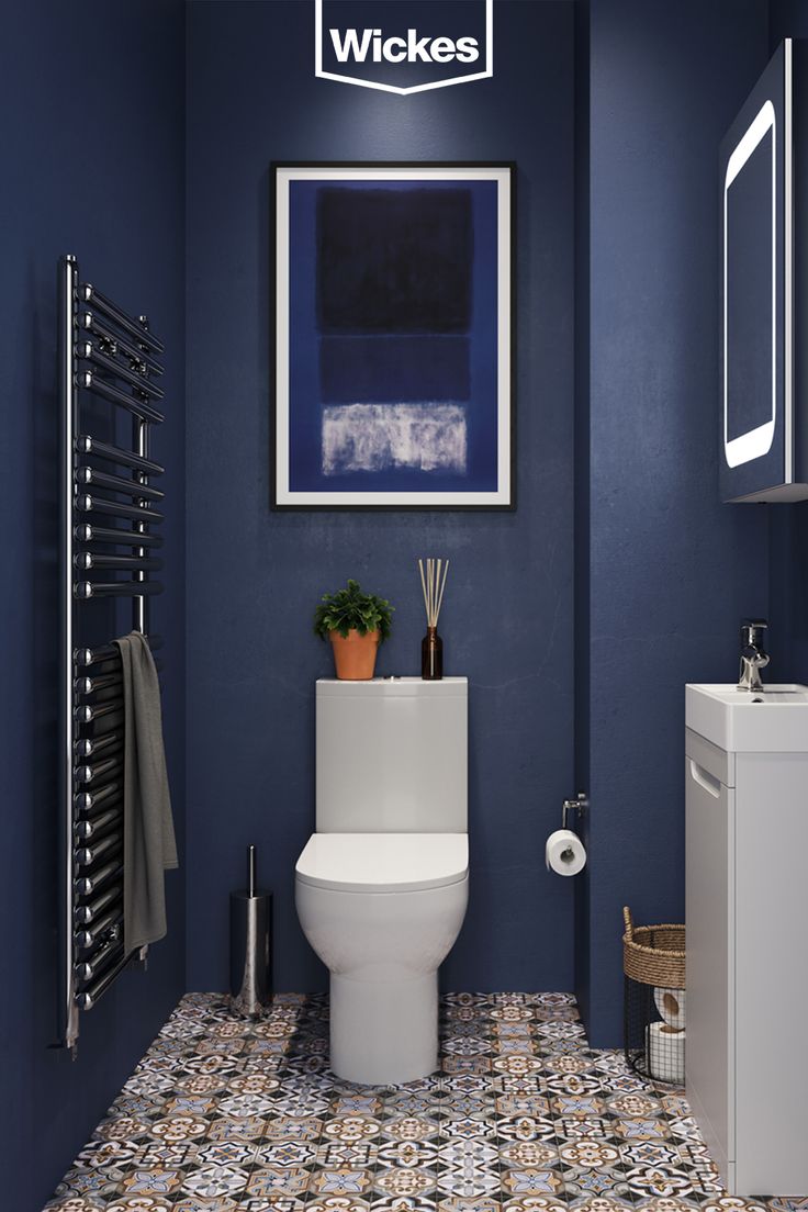 a bathroom with blue walls and tile flooring is pictured in this image, there is a toilet next to the sink