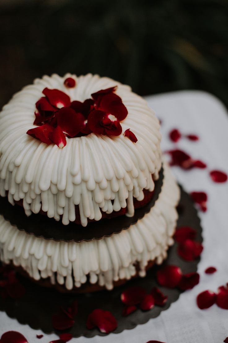 two cakes are stacked on top of each other with red petals scattered around the edges