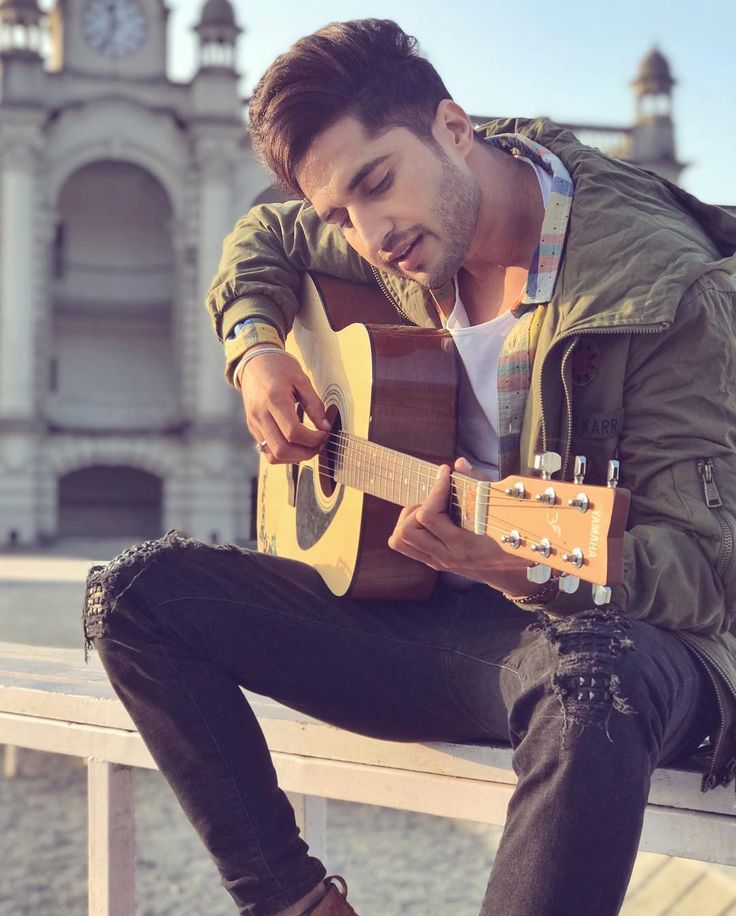 a man sitting on a bench playing an acoustic guitar