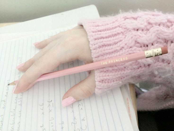 a woman's hand holding a pencil in her pink sweater