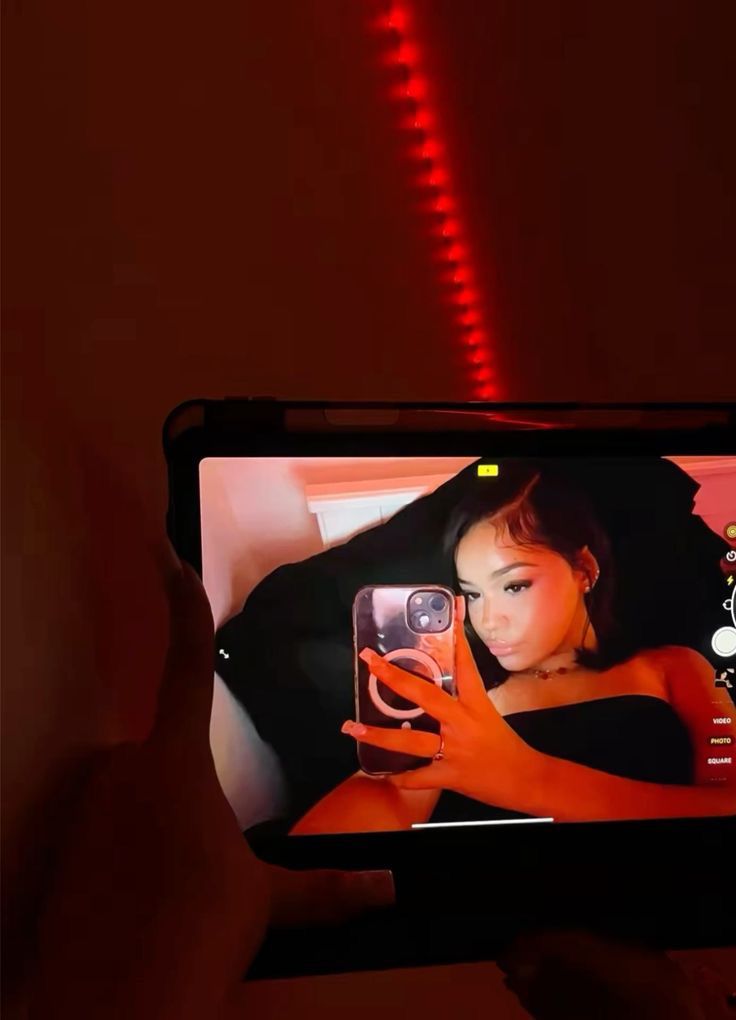 a person holding up a cell phone in front of a red light with the image of a woman on it