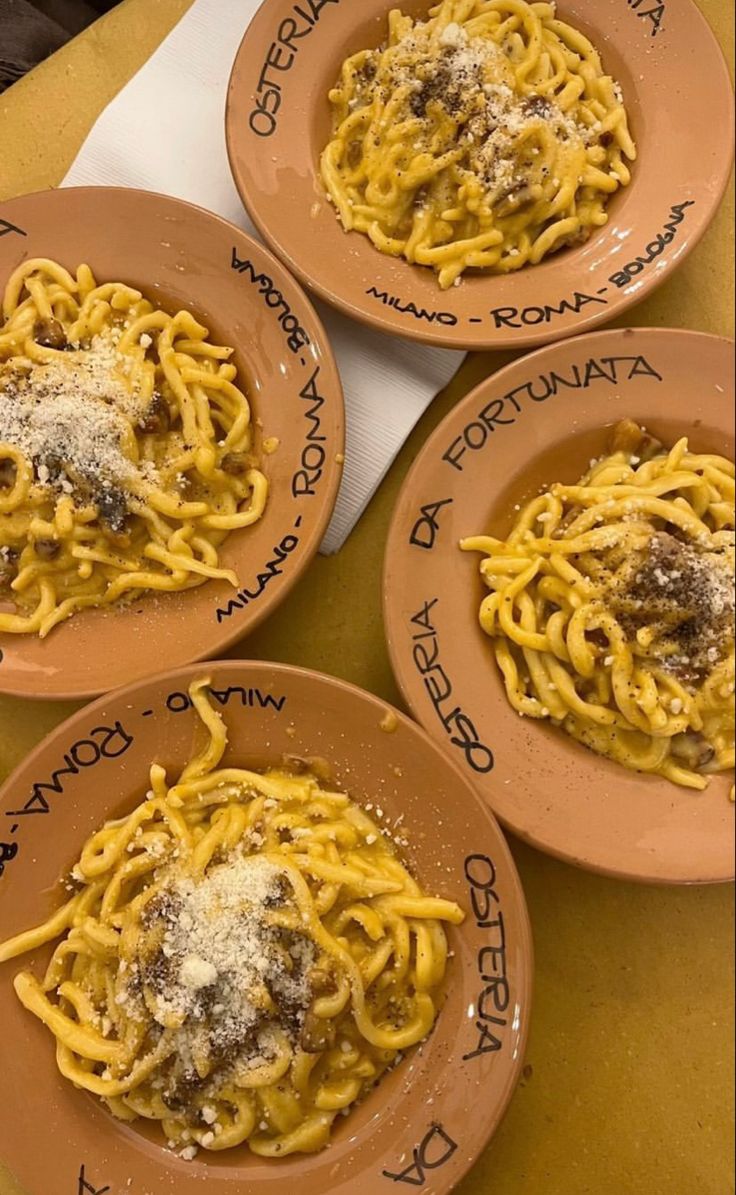 four plates of pasta with cheese and meat on them sitting on a yellow table cloth