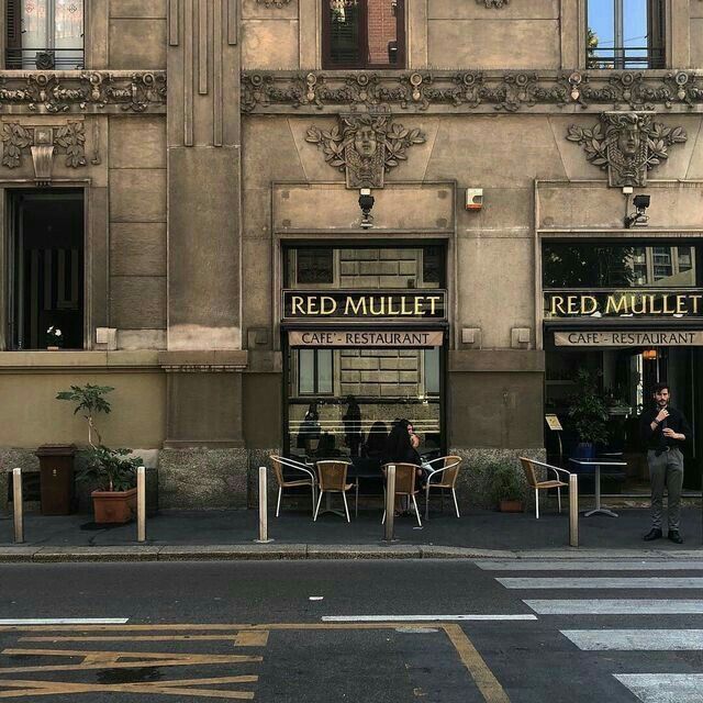 two people sitting at tables in front of a red mullet restaurant on a city street