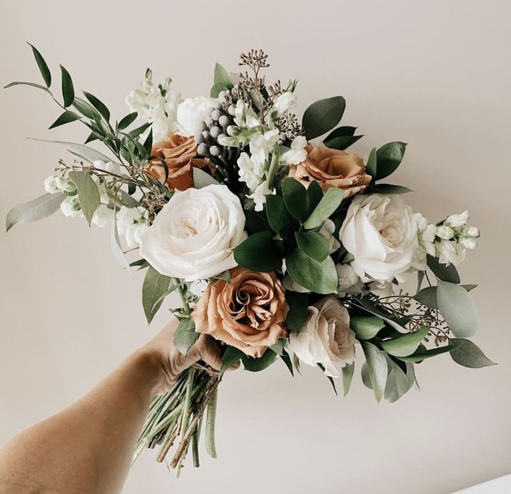 a person holding a bouquet of flowers in their hand with greenery on the side