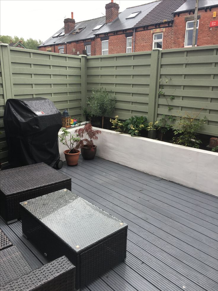 an outdoor deck with black furniture and potted plants on the other side, in front of a fence