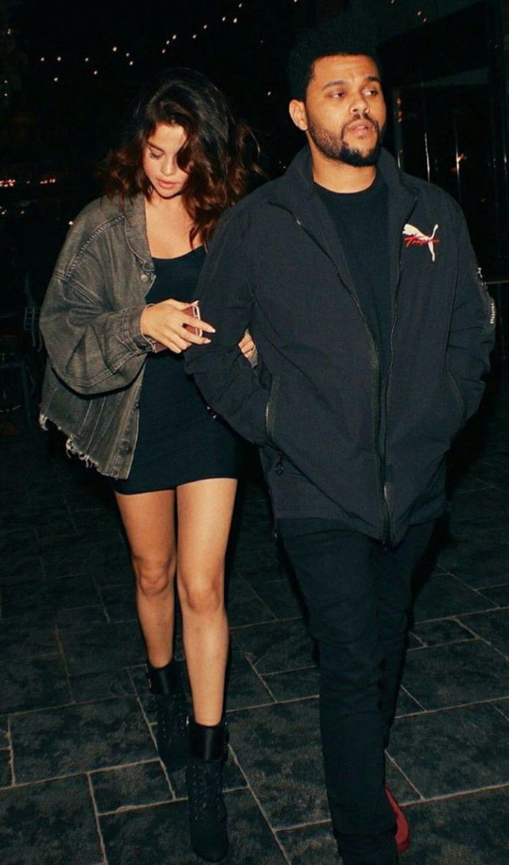 a man and woman are walking down the street at night together, both dressed in black