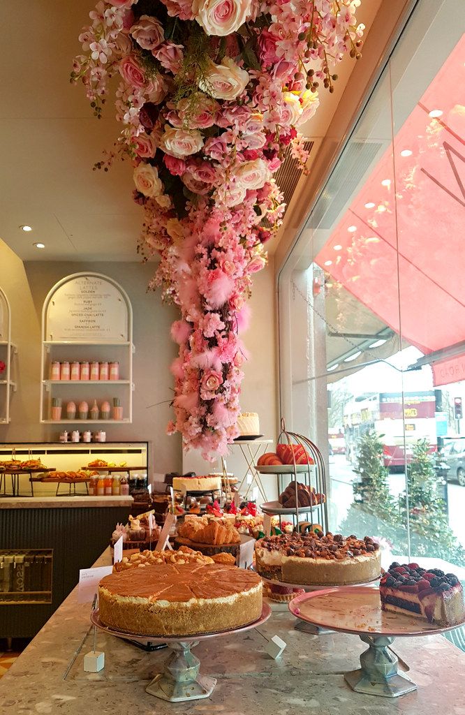 several desserts on display in a bakery with pink and white flowers hanging from the ceiling