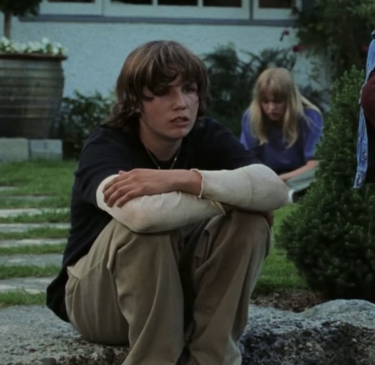 two young people sitting on rocks in front of a house with their arms folded out