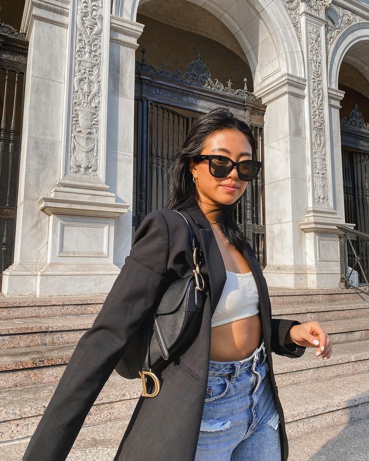 a woman wearing sunglasses and a black jacket is walking down the steps in front of a building