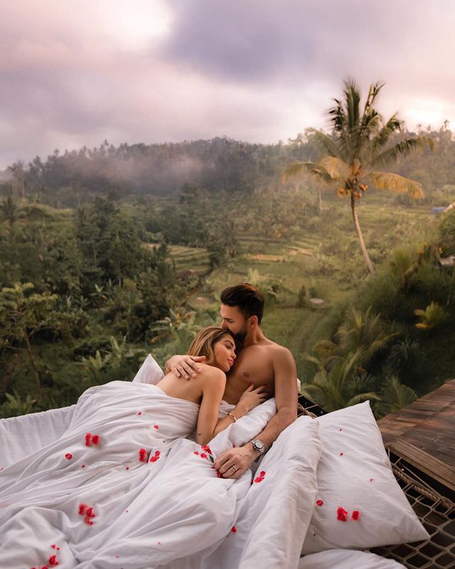 a man and woman are laying in bed with flowers on the sheets looking at each other