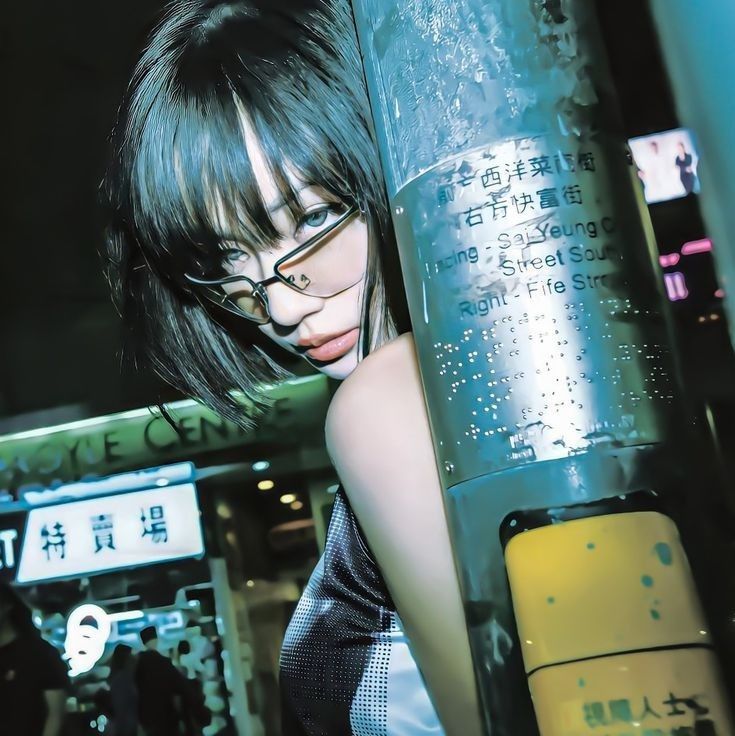 a woman with glasses leaning against a pole